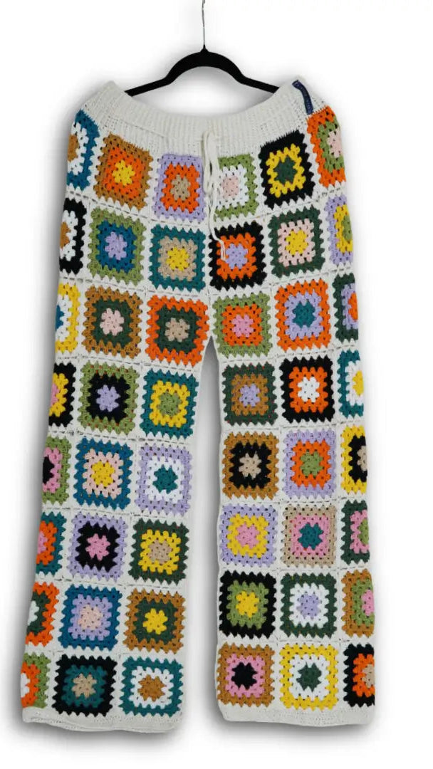 Colorful crocheted pants on a hanger against a white background