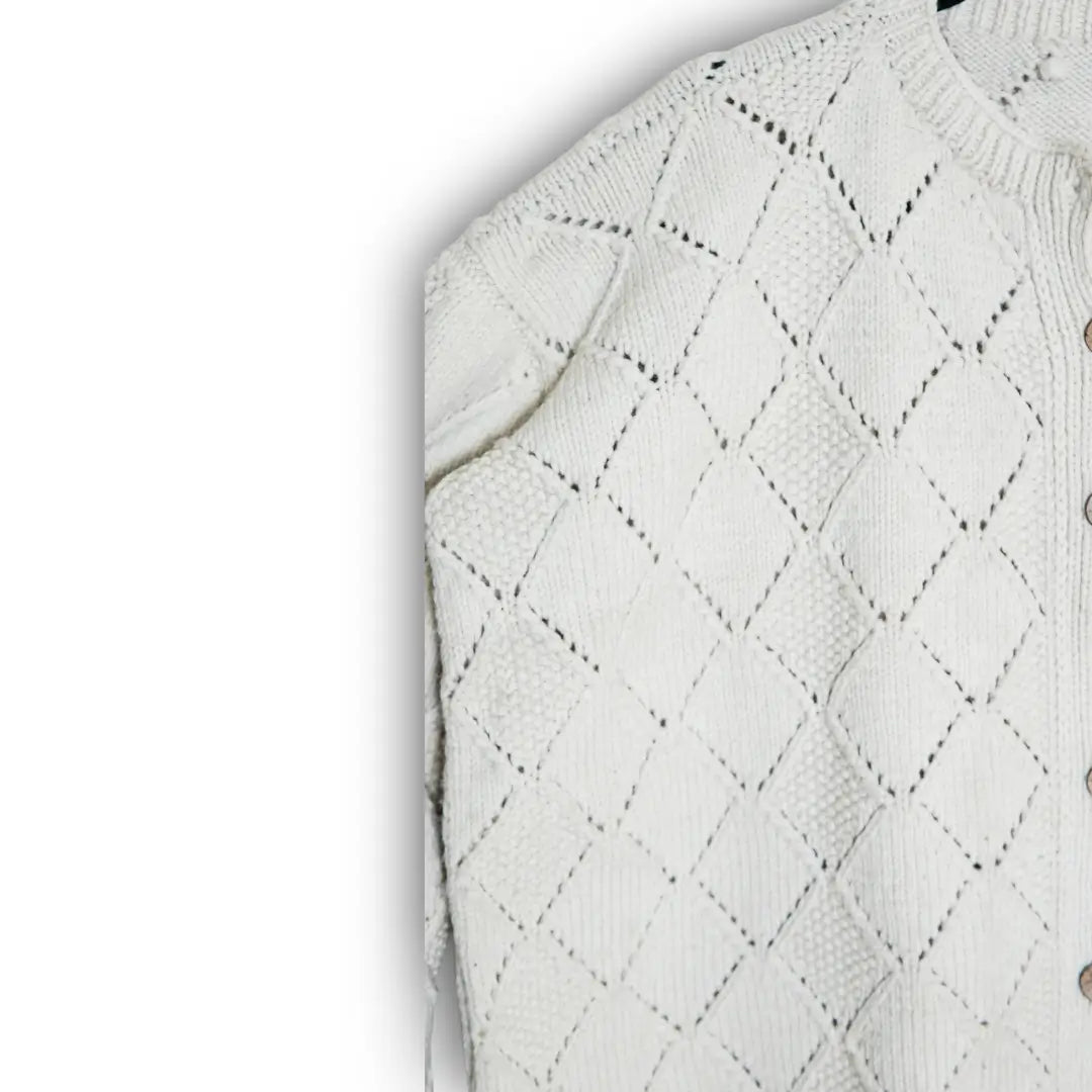Close-up of a white knitted sweater with diamond pattern on a light gray background
