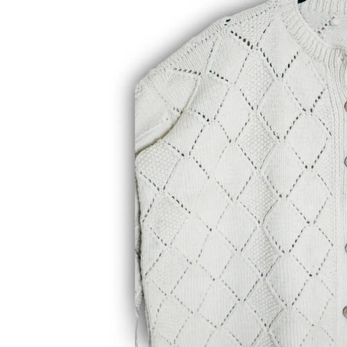 Close-up of a white knitted sweater with diamond pattern on a light gray background