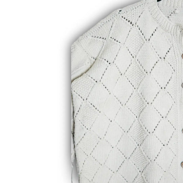 Close-up of a white knitted sweater with diamond pattern on a light gray background
